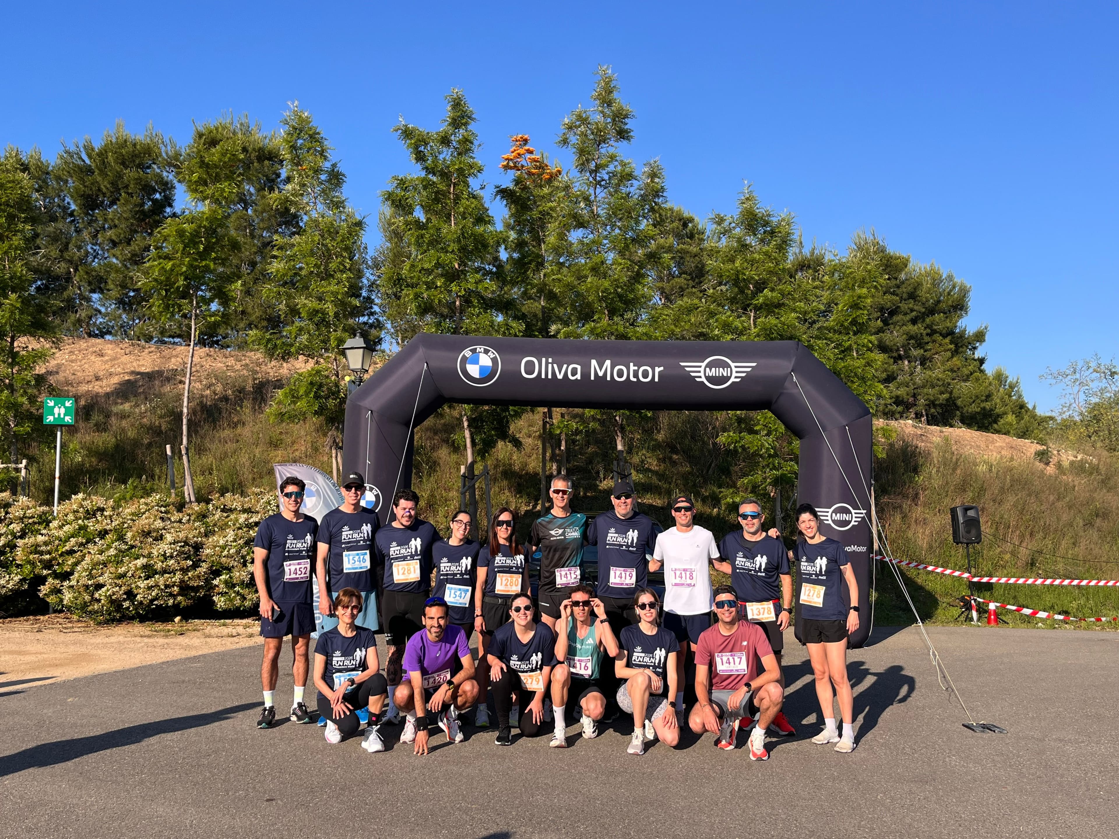 Fotografia de grup de l'equip de Grup Oliva Motor participant a la cursa Fun Run Corporate a PortAventura World, posant davant d'un arc inflable de BMW i MINI Oliva Motor.